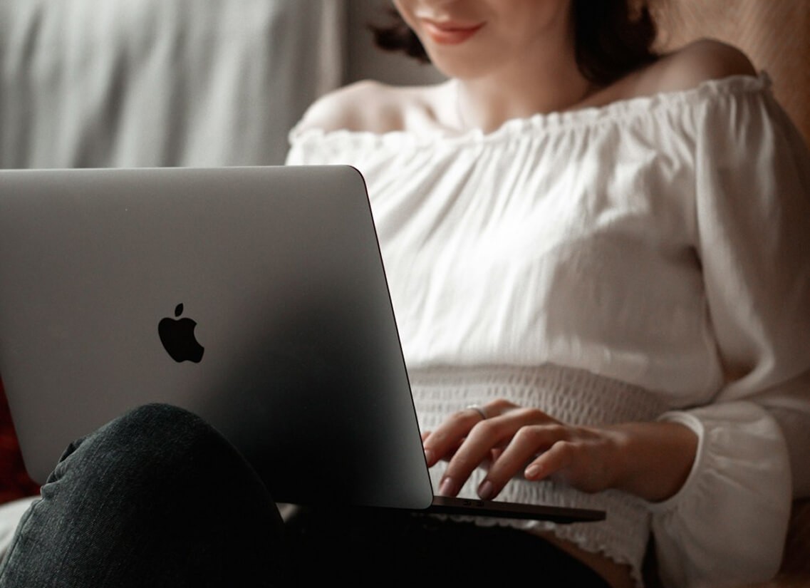 Person in a white off-shoulder top using a MacBook laptop, with text overlay 'What's new in knitwear?' and the inara sourcinglogo in the top corner.